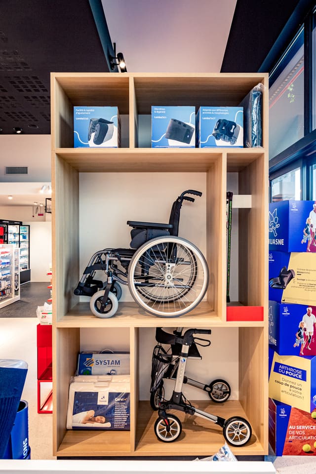 La bibliothèque orthopédie : casiers de bois clair présentant un fauteuil roulant et un déambulateur