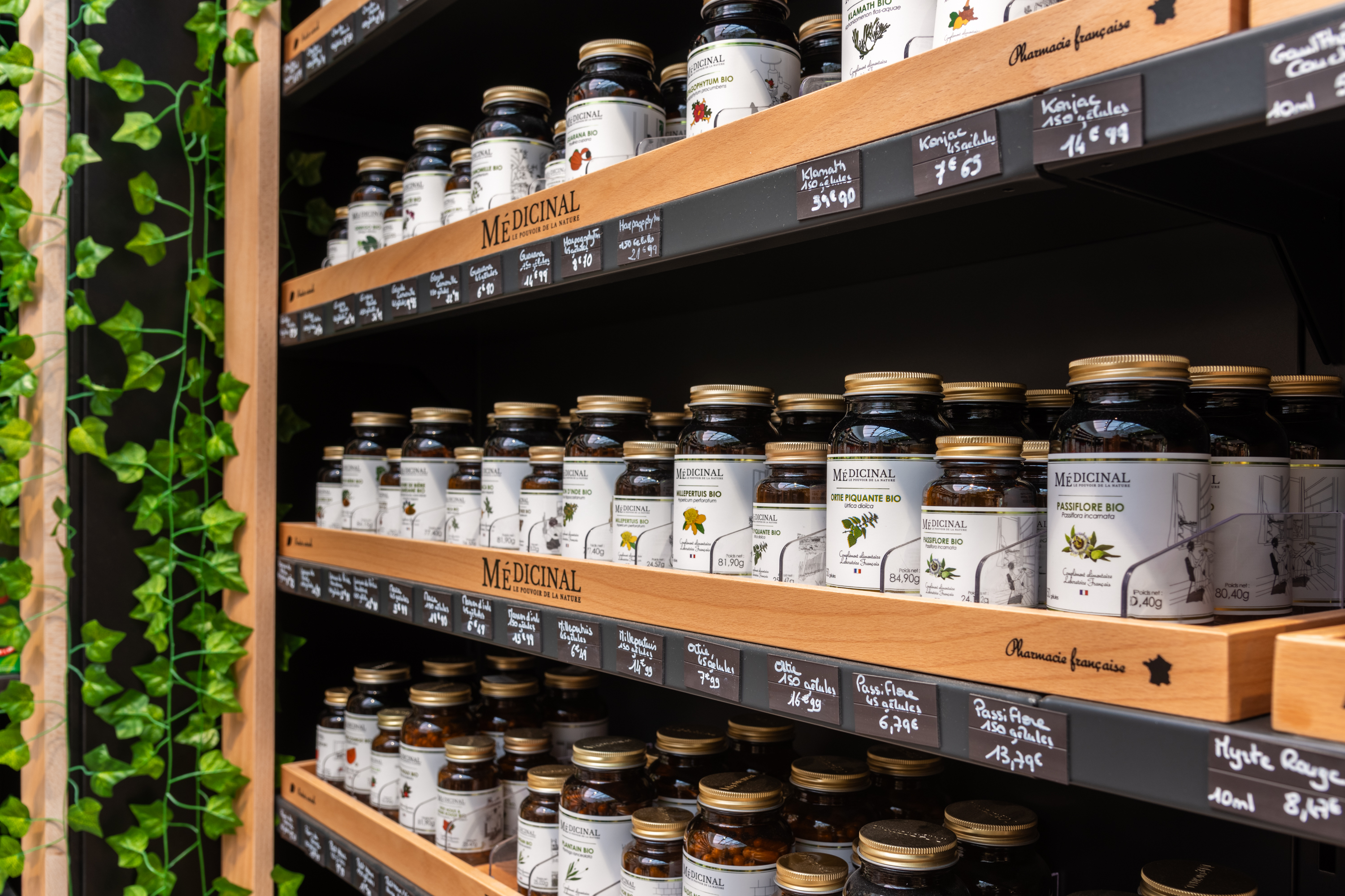 Rayon compléments alimentaires de la marque Médicinal en pharmacie française,  avec étiquettes de prix manuscrites et végétation murale décorative.